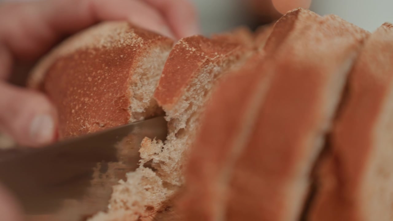 Mani che strappano una mollica da una fetta di pane su un tagliere di legno, interno morbido e crosta croccante rivelati da dita delicate, un'atmosfera calda e casalinga evoca il comfort di una lenta mattinata e un sottile sottofondo musicale per la quiete