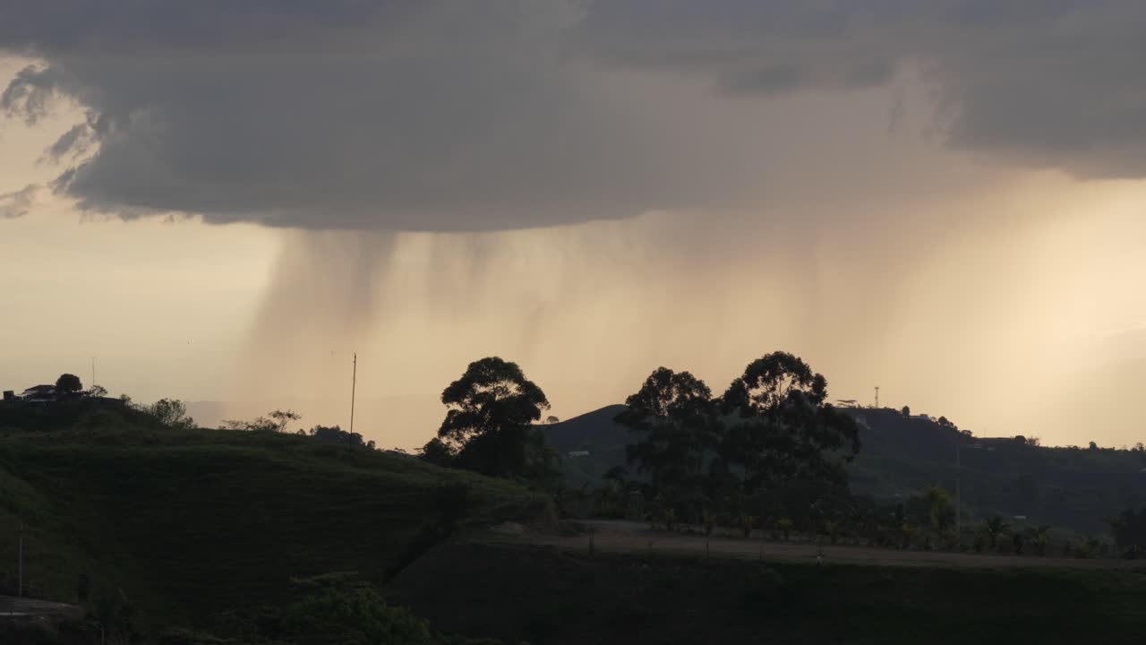 Distant rain curtains sweep past tree silhouettes over Filandia’s hills