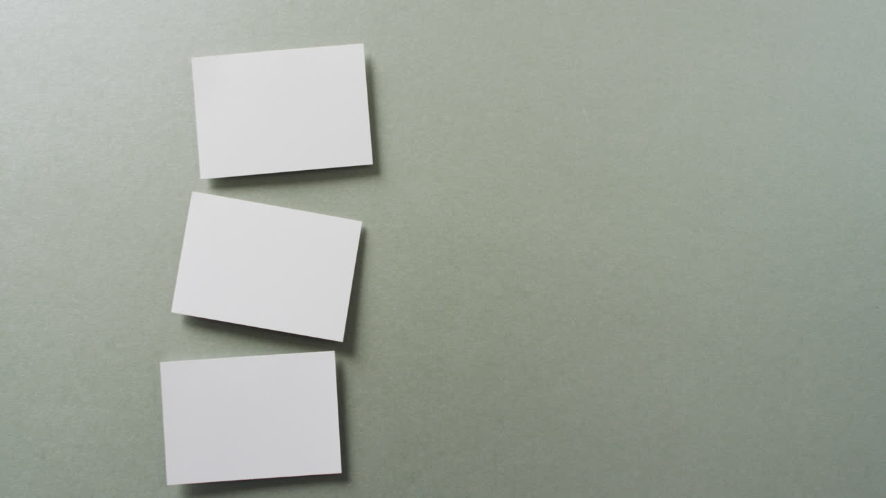 vista aérea de tres tarjetas de visita blancas dispuestas en fondo gris, espacio de copia, cámara lenta