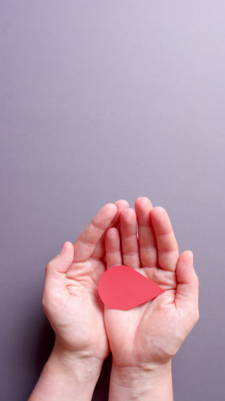 Vertical video of hands of caucasian man holding blood drop on grey background with copy space