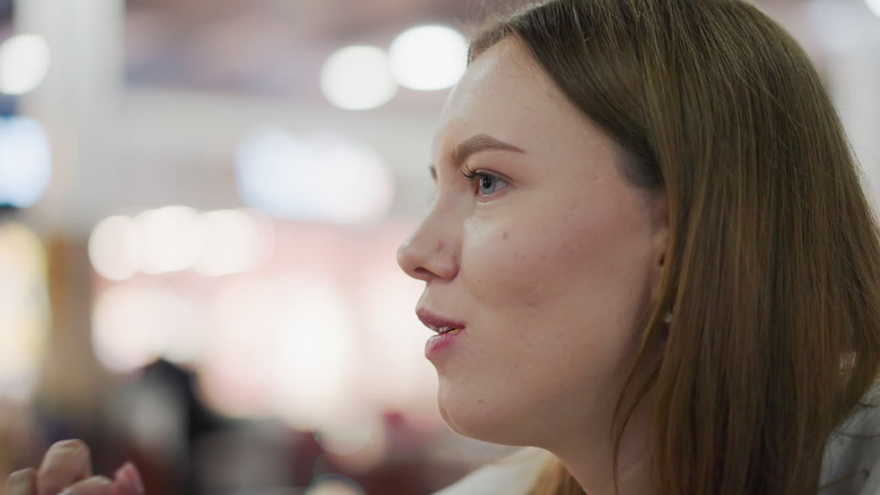 primer plano de una mujer con uñas pulidas disfrutando de papas fritas en un entorno interior vibrante, con iluminación cálida y detalles de fondo borrosos