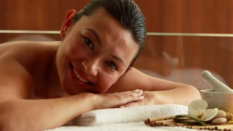 hermosa morena acostada en la mesa de masaje sonriendo a la cámara