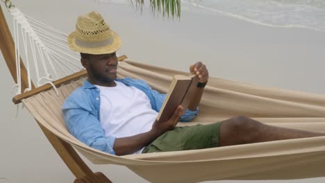 front view of african american man reading a book on the beach 4k