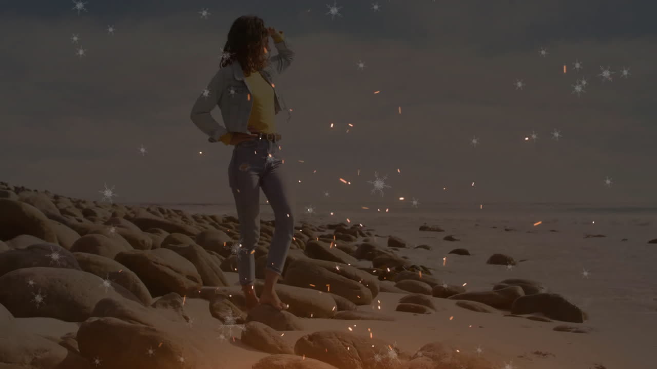 Woman shielding eyes on rocky shoreline, showcasing spark snowflake overlays for travel marketing