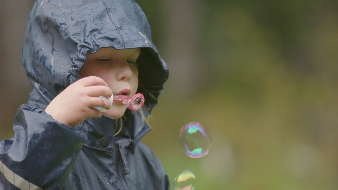 cámara lenta - lindo niño soplando burbujas bajo la lluvia