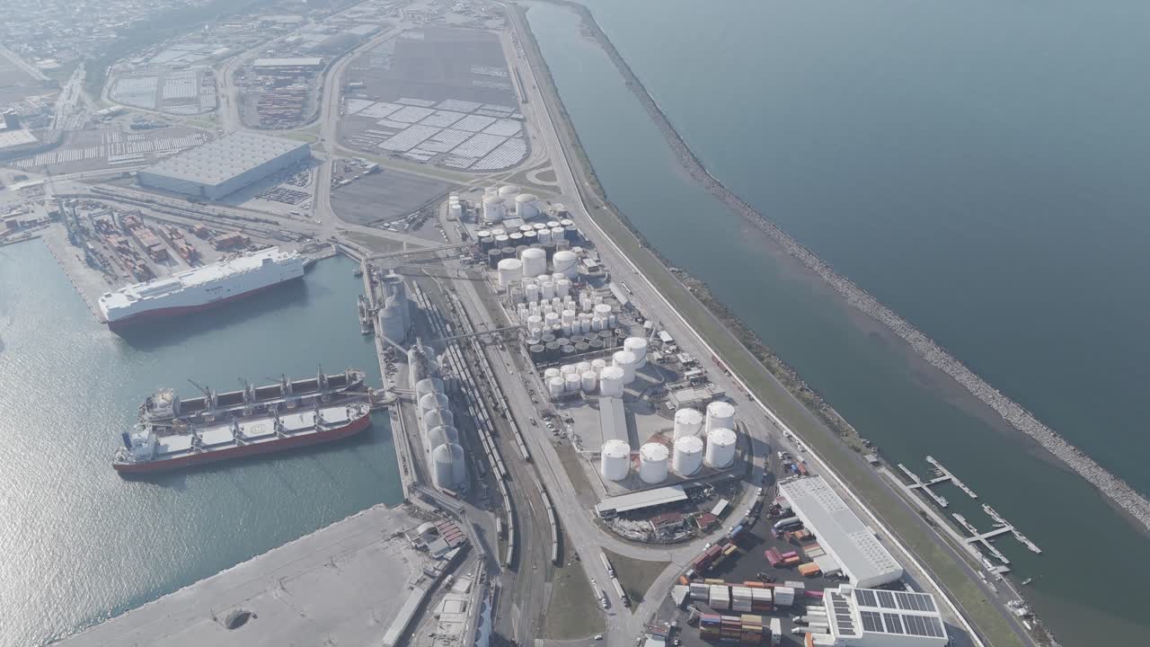 Aerial view of a petrochemical terminal by the ocean, with vessels docked nearby. A snapshot of maritime industry and energy infrastructure.