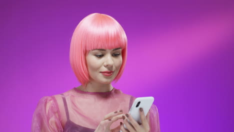 close up of stylish woman wearing a pink wig tapping and texting on mobile phone and reading message