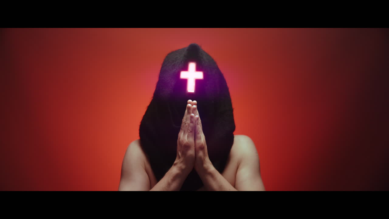 Masked man with cross of light glowing on his face prays - red background