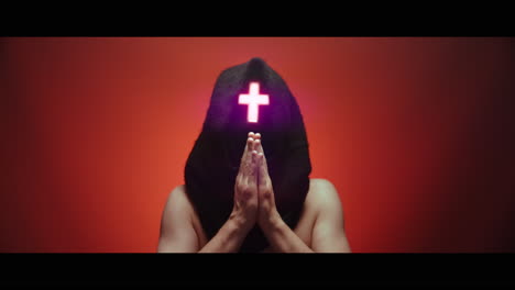 masked man with cross of light glowing on his face prays - red background