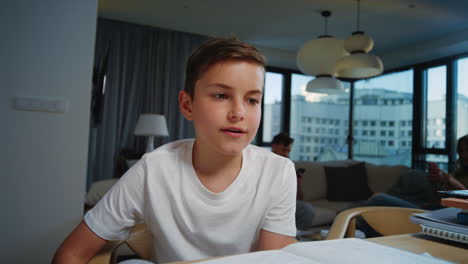 cute child looking camera indoors. smiling boy sitting at table at home.