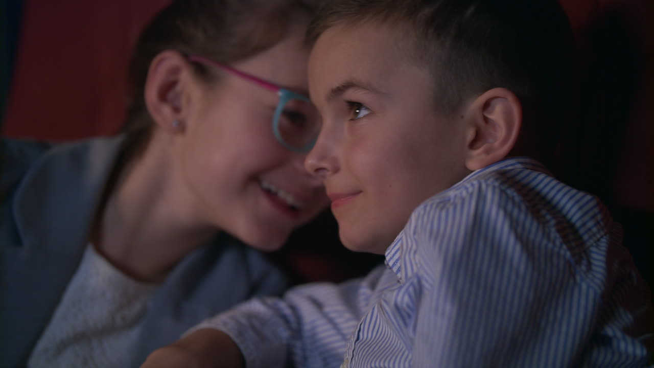 Pige hvisker til dreng, der ser film i biografen. Børnefilmunterholdning.