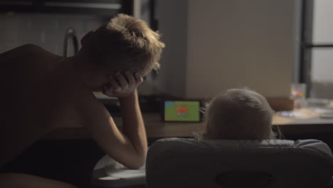 a back view of a boy and a baby girl watching cartoon on a tablet