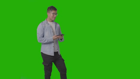 Studio-Shot-Of-Casually-Dressed-Smiling-Man-Wearing-Glasses-Talking-On-Mobile-Phone-Against-Green-Screen-