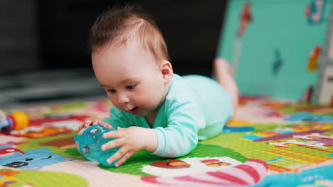 charming baby with funny hairstyle lies on mat. nice kid is playing with a bottle trying to take it in his mouth. close up.
