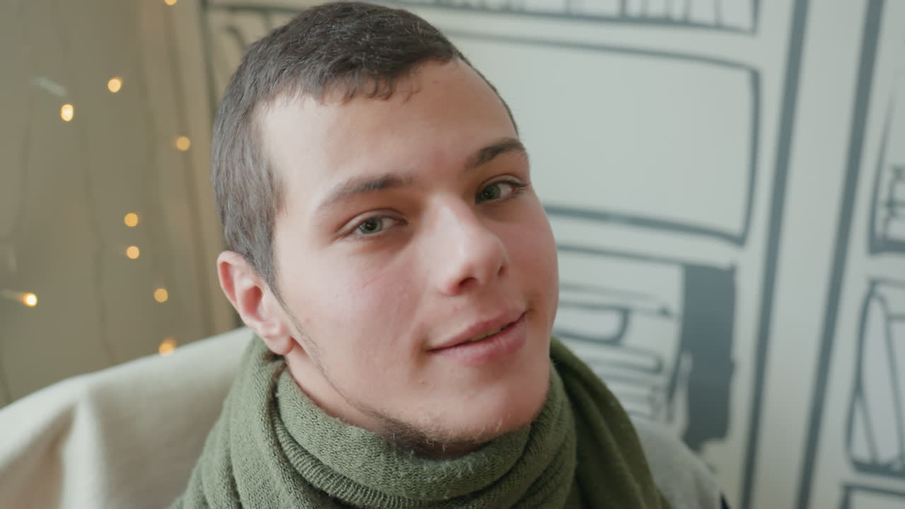 Uomo bianco si mette gli occhiali da sole, ritratto indoor sicuro di sé con carta da parati a libreria e lucine fatate, giovane uomo bianco si sistema gli occhiali con atteggiamento calmo, sciarpa e maglione eleganti, modello e influencer