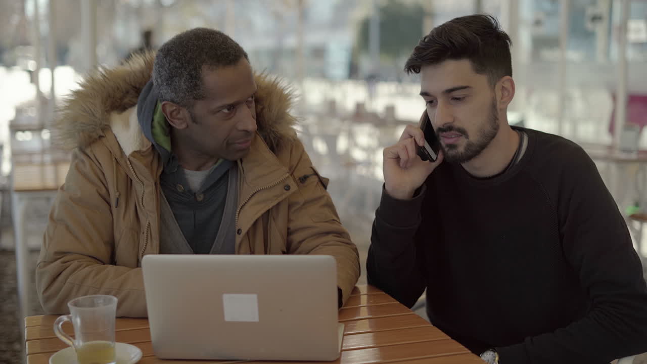 Multiethnic men using laptop and cell phone in cafe