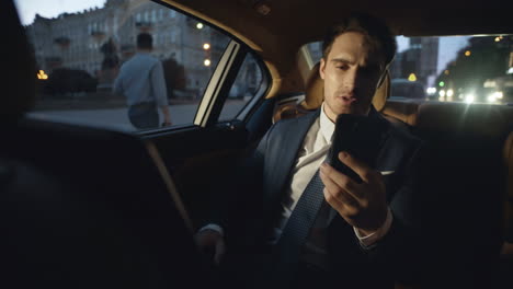 Tired-male-professional-speaking-on-video-call-on-smartphone-in-dark-luxury-car.