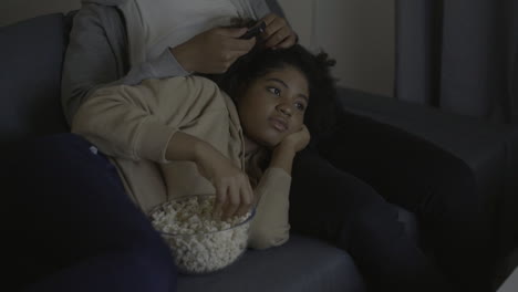 young woman watching a movie and eating popcorn leaning on her boyfriend's lap