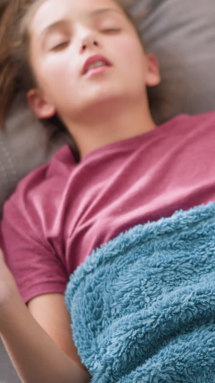 Primo piano di una donna debilitata che si sistema sotto una morbida coperta blu, circondata da fazzoletti, che mostra segni di malattia e affaticamento, indicando sintomi di raffreddore o influenza con un fazzoletto su di lei