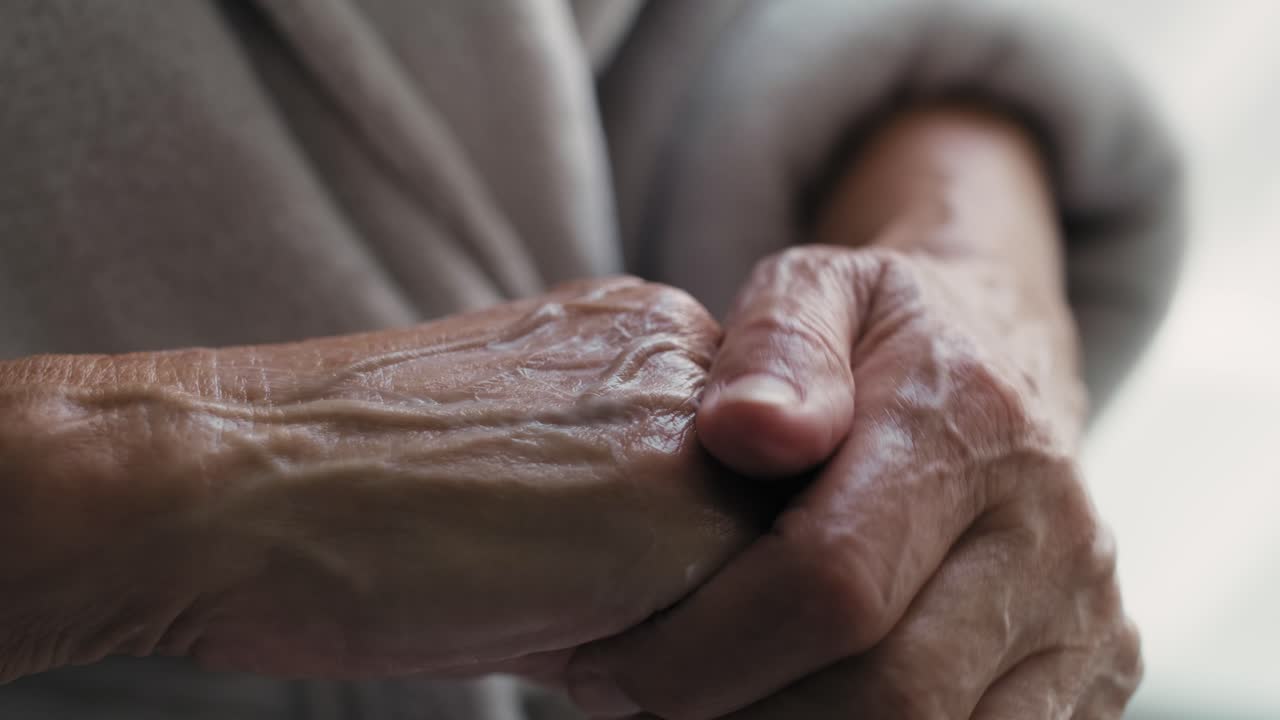 Detalhe de mulher idosa aplicando creme hidratante nas mãos.