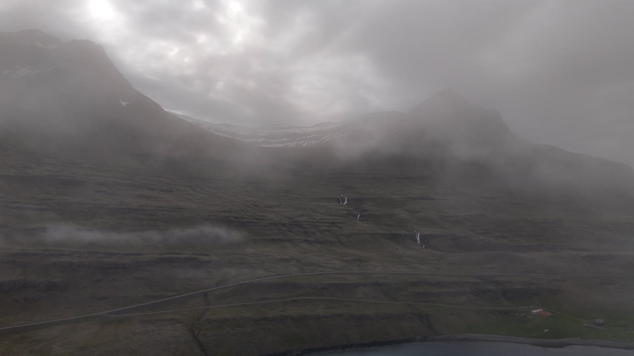 Misty mountain slopes and small waterfalls overlook Berufjörður as drifting clouds slide across the rugged Icelandic landscape