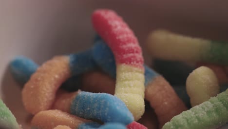 varied colors of gummy worms with confectionery sugar in a white bowl