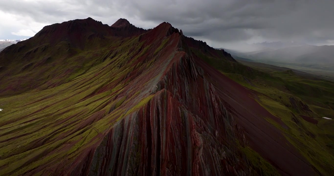 Cresta a strisce colorate si erge sotto nuvole scure a Pallay Punchu Rainbow Mountain, Perù, con il drone che si sposta a sinistra creando ombre drammatiche e canali definiti.