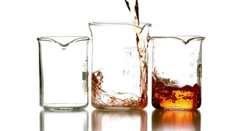 Orange-liquid-pouring-into-three-beakers