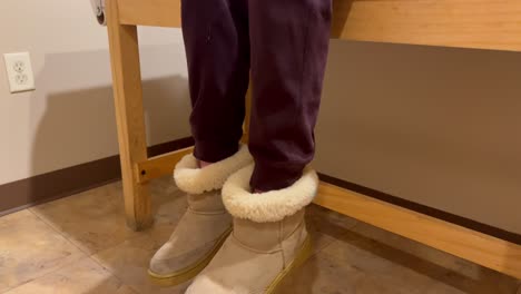 young kid child girl or boy in covid-19 mask at doctor’s office hospital visit waiting on examination table nervously fidgeting kicking feet semi-close shot panning down on ugg slipper shoes feet.