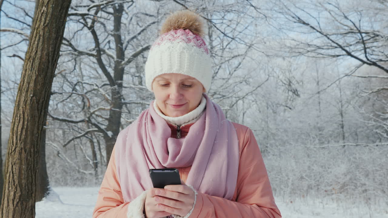 겨울 공원에서 산책하는 젊은 여성은 스마트폰 4k 슬로우 모션 비디오를 즐깁니다.