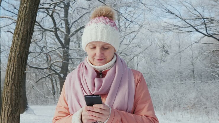 Giovane donna cammina in un parco invernale e usa lo smartphone. Video 4K in slow motion