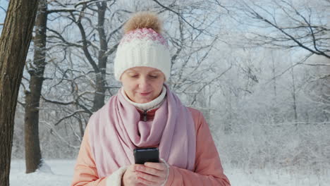 young woman walks in winter park enjoys smartphone 4k slow motion video