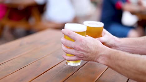 two hands lifting beer glasses off a table