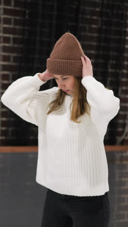 una vista cercana de una mujer patinando tranquilamente en una pista de hielo, moviéndose lentamente mientras coloca su mano sobre su cabeza, lleva un suéter blanco y una gorra marrón