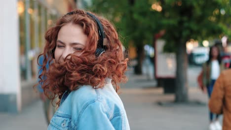 redheaded woman in headphones listening to the music with smartphone and dancing in the street