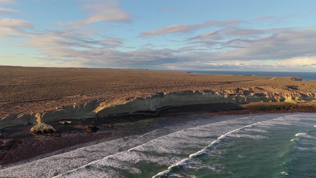Et sveipende luftfoto med drone som fanger de dramatiske kystklippene og den enorme tørre steppen som møter det dypblå Atlanterhavet i Puerto Madryn, Argentina