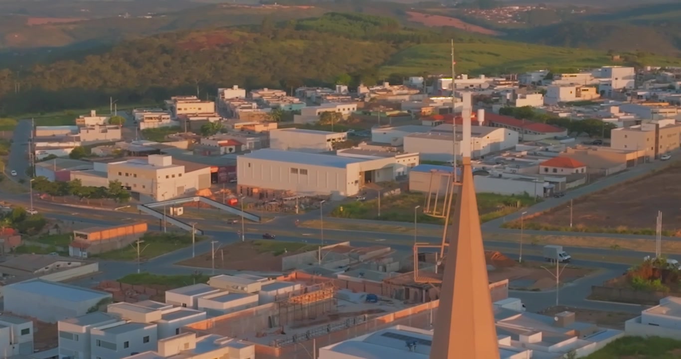 Campanile della chiesa che si erge sopra il centro di Santo Antônio do Monte, Minas Gerais, Brasile, con l'autostrada MG-164 e le dolci colline sullo sfondo alla luce del tramonto, ripresa aerea con drone
