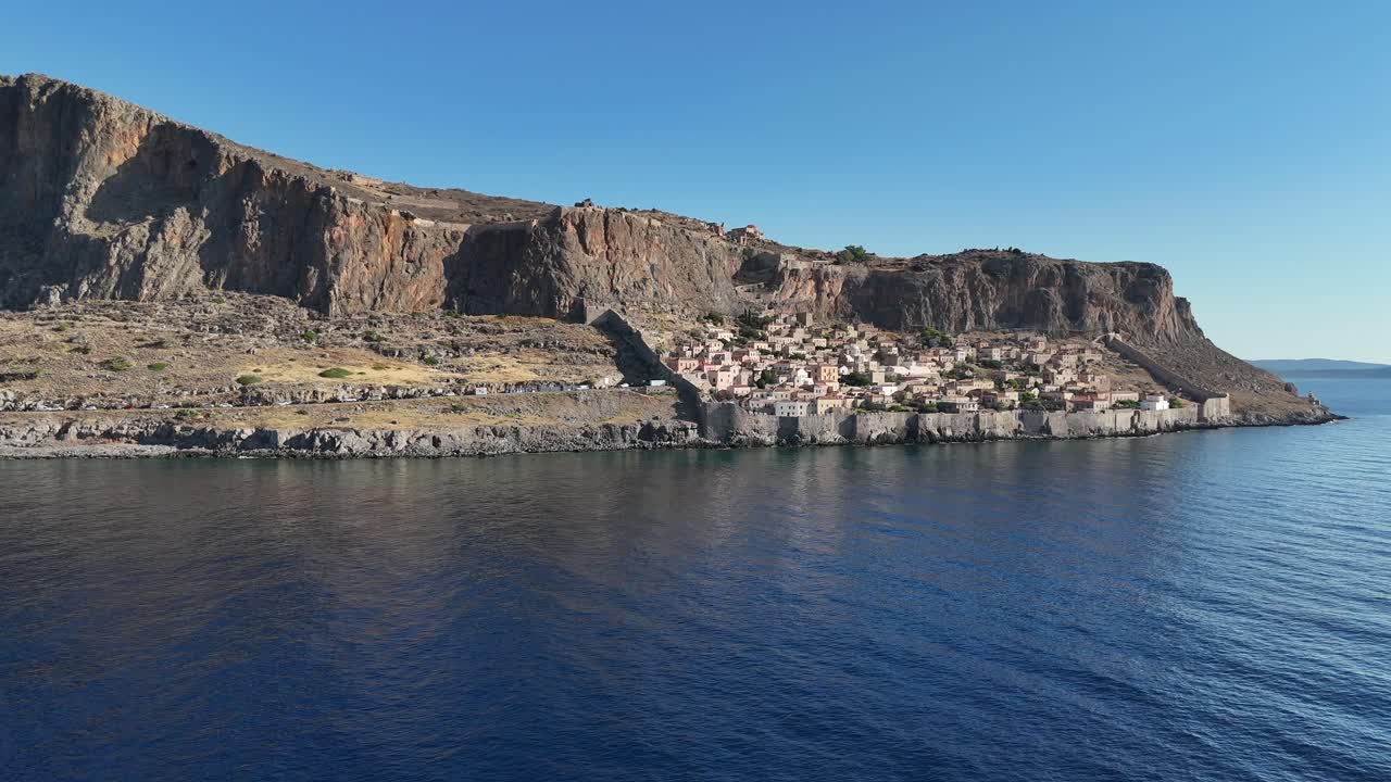 Peloponnese, Monemvasia, güneşli bir günde sakin denizler ve mavi gökyüzü eşliğinde eski kalenin yukarı ve aşağı kasabasını yavaşça kaplayan, sağa doğru kayan havadan kuş bakışı