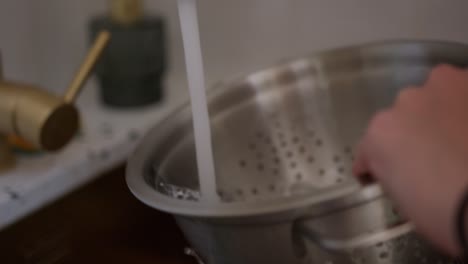 person washing steel strainer sieve metal bowl in sink, close up