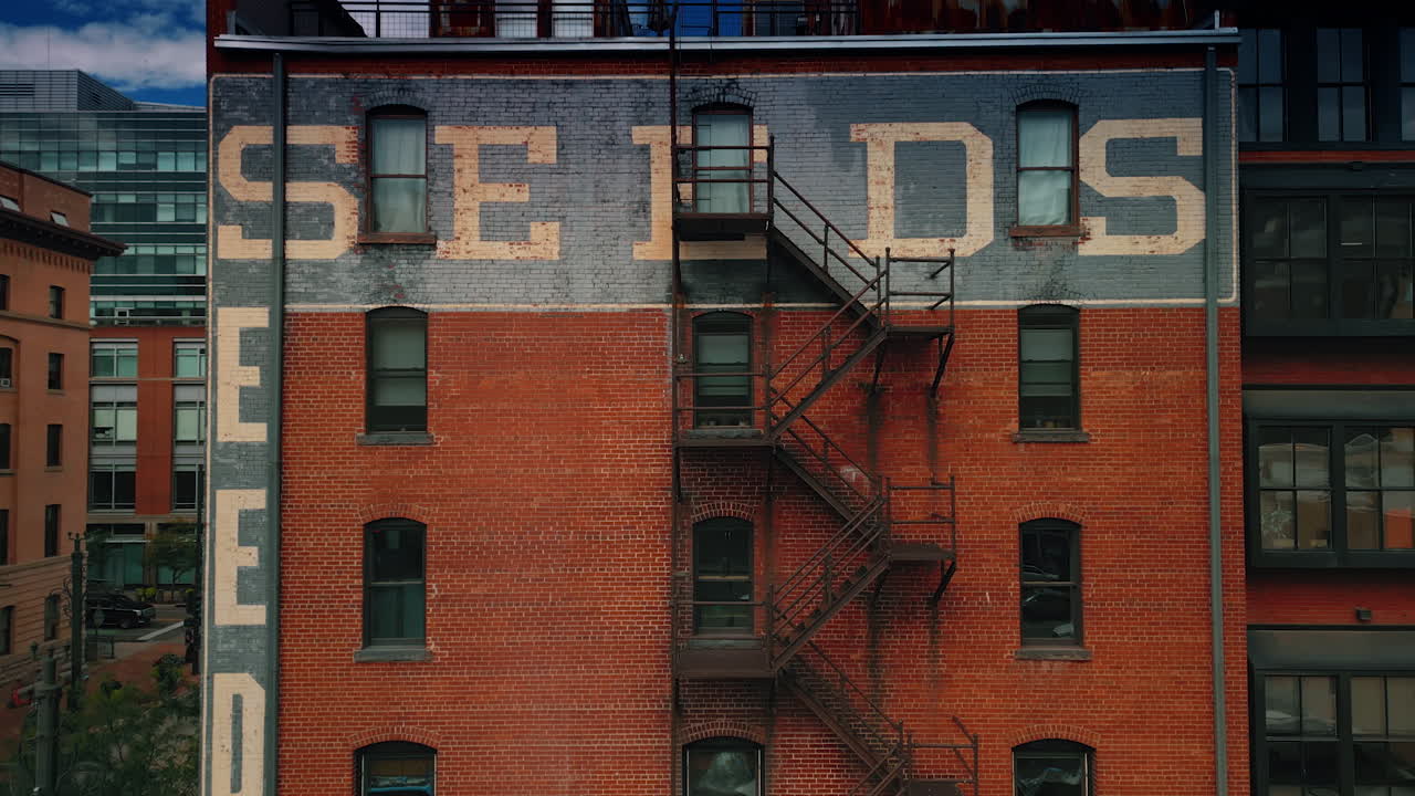 Denver, USA, 28 July 2025: Façade of the multi-storied red brick building with words "seeds" on the wall and fire escape ladder. Rising to the top of the structure with some annexes on the roof. Denver, Colorado, USA