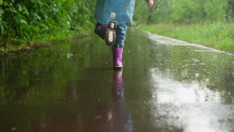 una niña camina a través de un charco en la lluvia, con botas de lluvia