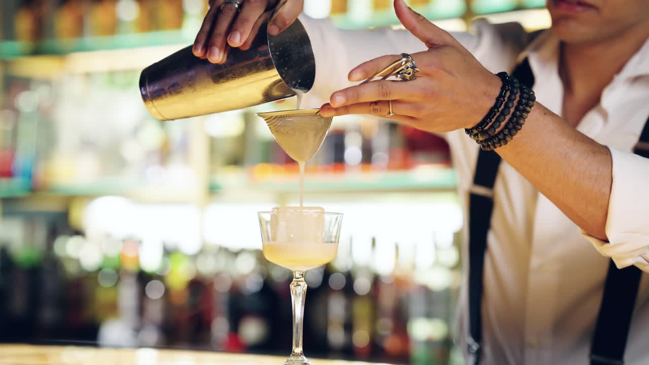 Bartender hælder en cocktail fra shaker i et glas på en bar