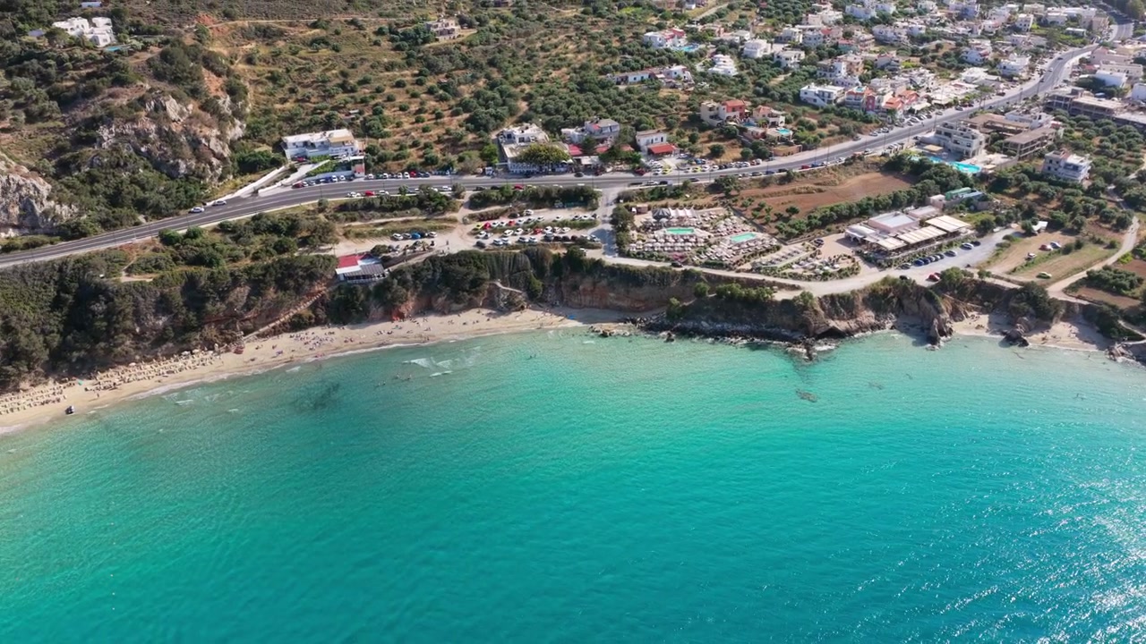 Yunanistan'daki Voulisma Plajı'nın, yamaçtaki bir tatil kasabasının altında yer alan, turkuaz renkli koyu ve şemsiyelerle kaplı kumlu plajının havadan drone görüntüsü.