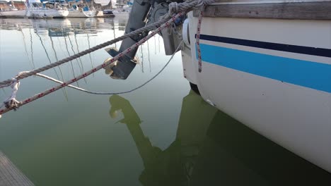 back of a yacht with an outboard motor tied with ropes to a walk-on mooring slightly rocking as the water moves below in a marina club