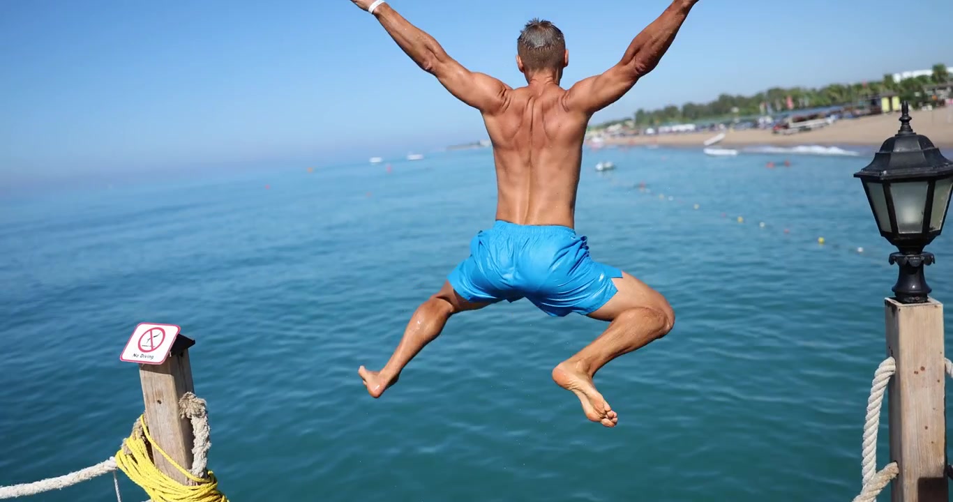 Homem de sunga azul corre e pula energicamente no mar
