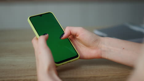 woman holding greenscreen smartphone scrolling touchscreen at home close up.