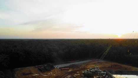 Cinematic-4K-Drone-Footage-of-Onshore-Drilling-Rig-equipment-structure-for-oil-exploration-and-exploitation-in-the-middle-of-jungle-surrounded-by-palm-oil-trees-during-sunset-and-high-oil-price