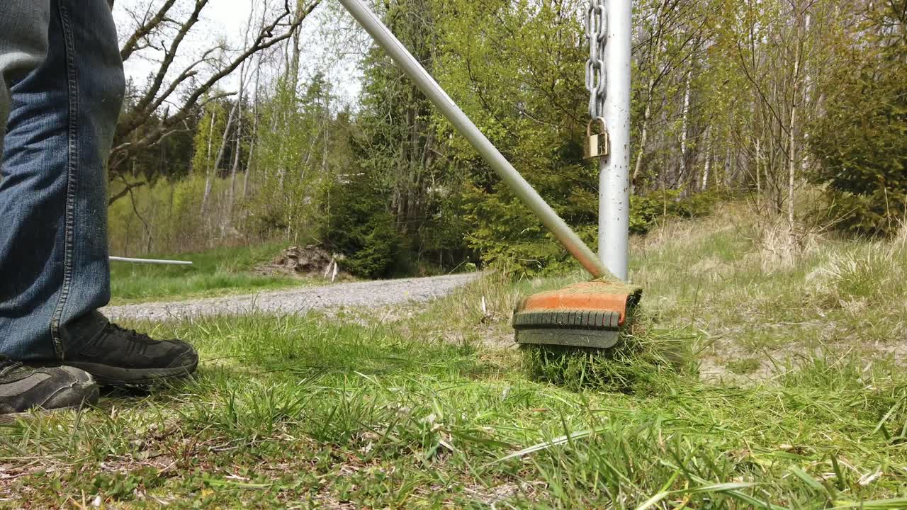 주황색 잔디 트리머로 잔디를 자르는 남자, 중간 샷 로우 프로파일