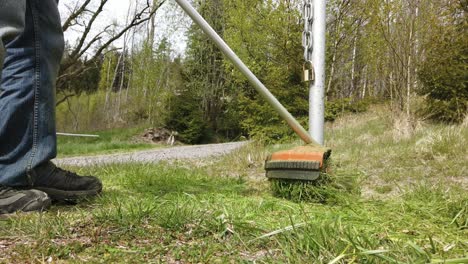 mann, der gras mit orangefarbenem rasentrimmer schneidet, mittlerer schuss, niedriges profil