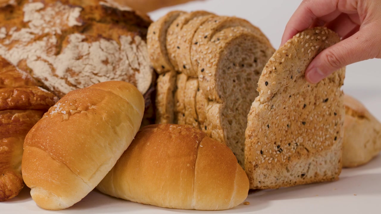 A hand selects sliced whole wheat bread from a variety of fresh bakery loaves.